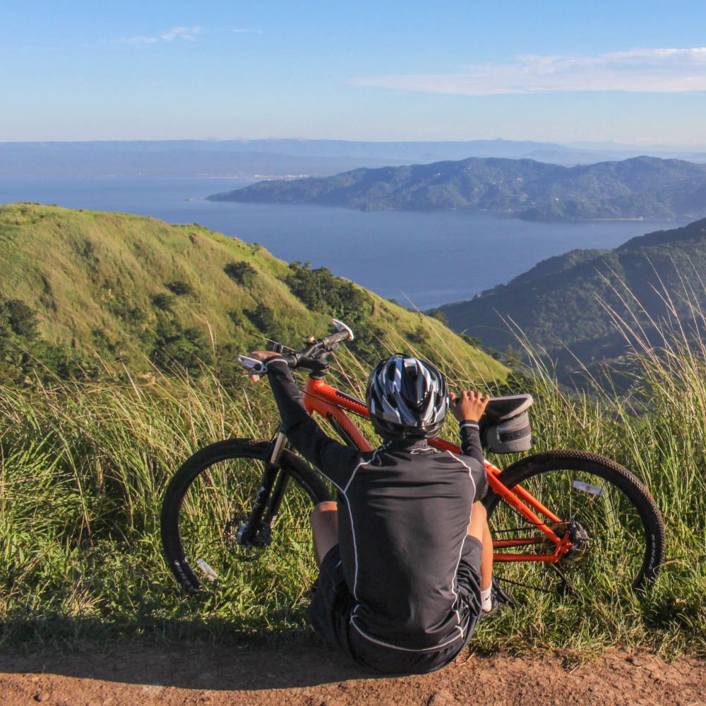 Füllbild: Fahrradfahrer sitzt mit seinem Rad vor einer schönen Landschaft.