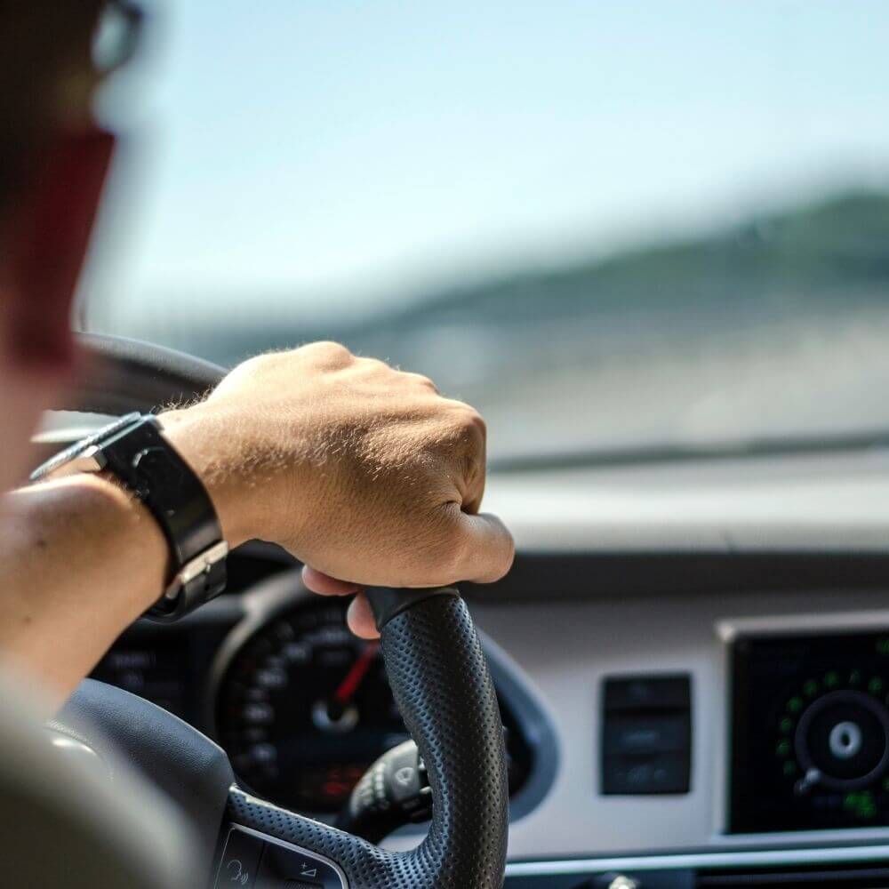 Füllbild: Person beim Autofahren über die Schulter fotografiert (Hand am Steuer).